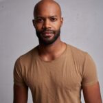 Daniel Gaymon smiling for professional headshot in beige t-shirt with a grey background.