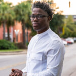 Film producer, Sherard Duvall, poses for a professional headshot in all white outside in an urban environment